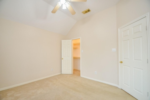 unfurnished bedroom featuring ceiling fan, light colored carpet, a spacious closet, and vaulted ceiling