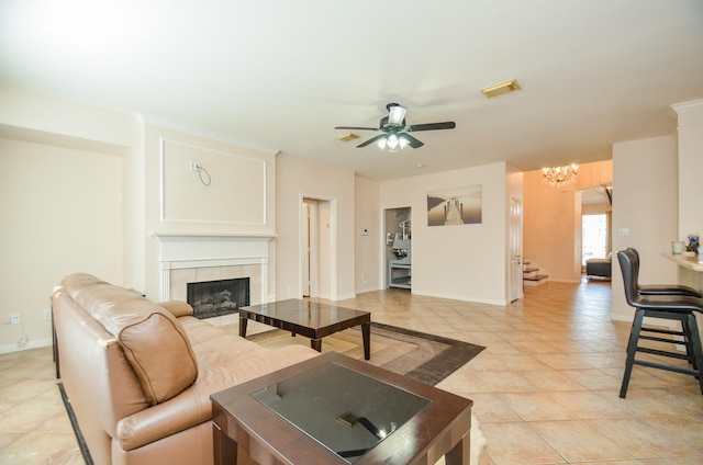 tiled living room with a tiled fireplace and ceiling fan with notable chandelier