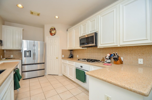 kitchen featuring light tile patterned floors, light stone countertops, appliances with stainless steel finishes, tasteful backsplash, and white cabinetry