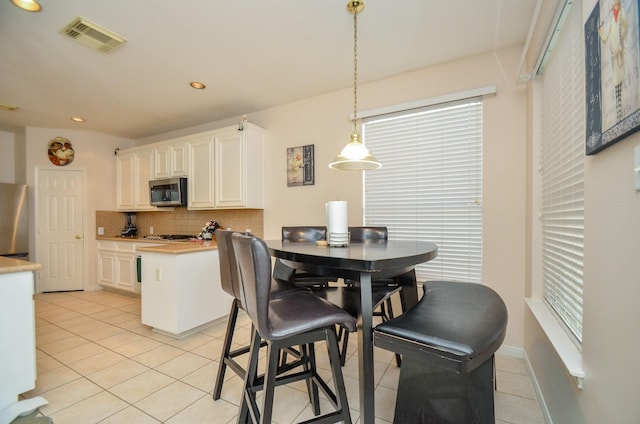 kitchen featuring appliances with stainless steel finishes, backsplash, light tile patterned floors, white cabinetry, and hanging light fixtures