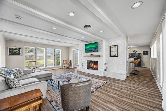 living room with beamed ceiling, wood-type flooring, a textured ceiling, and a brick fireplace