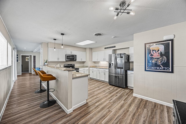 kitchen featuring hardwood / wood-style floors, white cabinets, pendant lighting, and appliances with stainless steel finishes