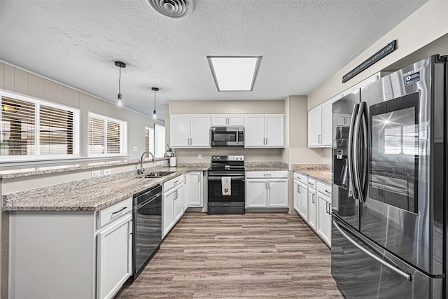 kitchen featuring pendant lighting, white cabinets, sink, light hardwood / wood-style floors, and stainless steel appliances