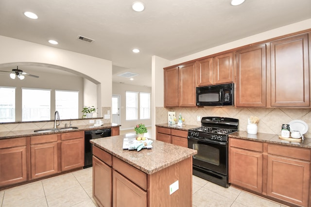 kitchen featuring black appliances, sink, light tile patterned floors, a kitchen island, and light stone counters