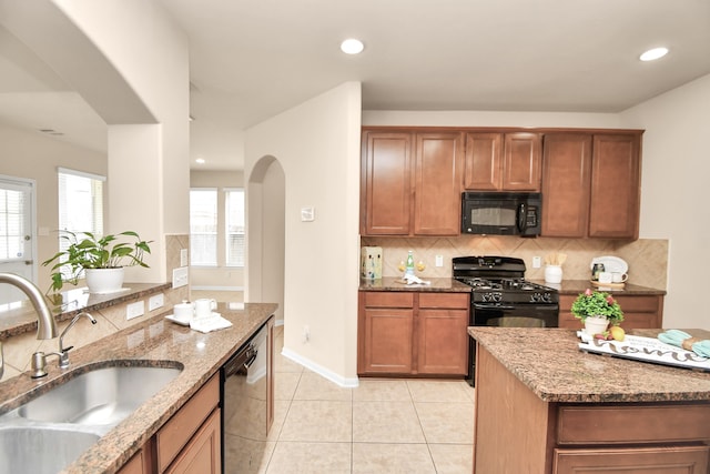 kitchen featuring black appliances, backsplash, light stone counters, and sink