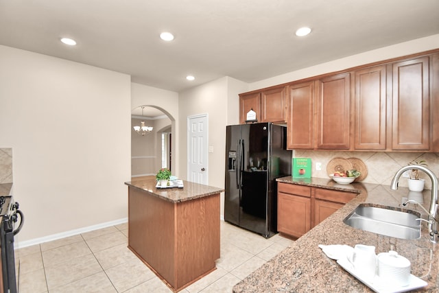 kitchen featuring tasteful backsplash, light stone counters, black refrigerator with ice dispenser, sink, and a center island