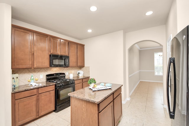 kitchen featuring light stone countertops, tasteful backsplash, black appliances, light tile patterned floors, and a kitchen island