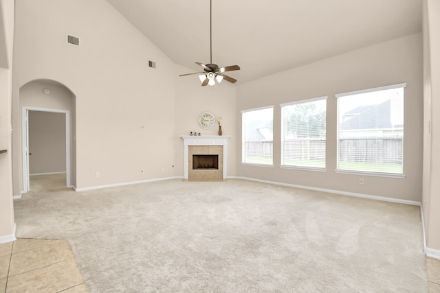 unfurnished living room featuring light colored carpet, high vaulted ceiling, ceiling fan, and a tiled fireplace