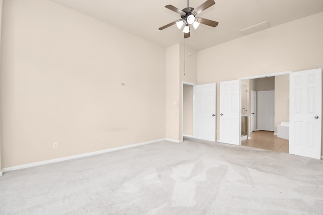 unfurnished bedroom featuring ceiling fan, light carpet, and a high ceiling