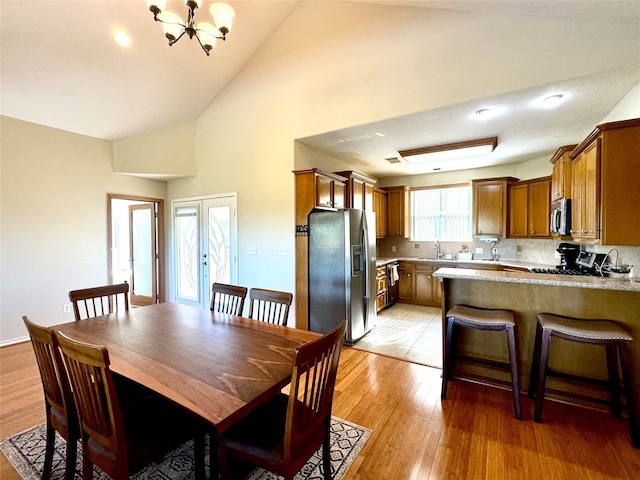 dining space featuring sink, high vaulted ceiling, light hardwood / wood-style floors, and an inviting chandelier