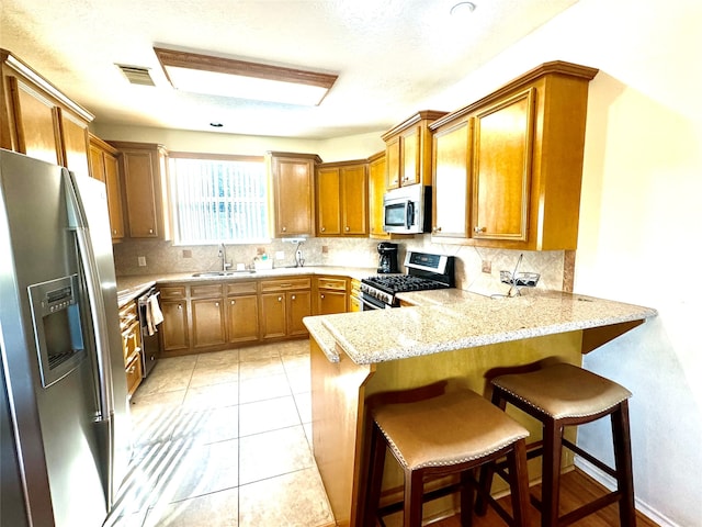 kitchen with kitchen peninsula, appliances with stainless steel finishes, a kitchen bar, backsplash, and sink