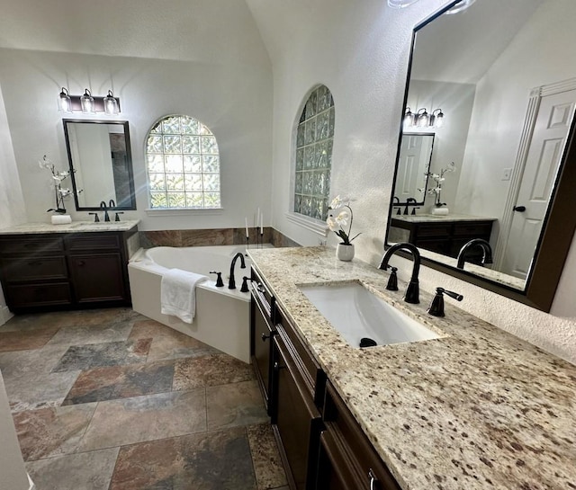 bathroom with vanity, vaulted ceiling, and a tub