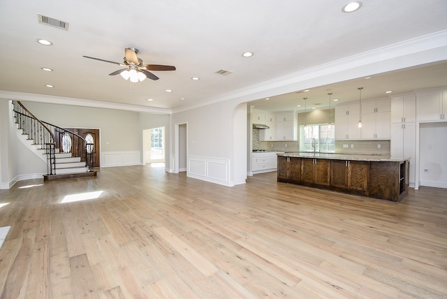 unfurnished living room featuring ceiling fan, sink, light hardwood / wood-style floors, and ornamental molding