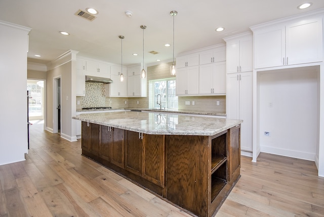 kitchen featuring white cabinets, a kitchen island, ornamental molding, and light hardwood / wood-style flooring