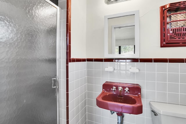 bathroom with sink, a shower with shower door, tile walls, and toilet