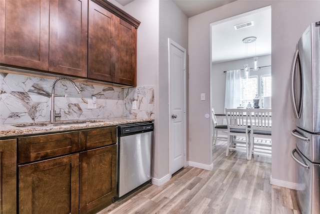 kitchen featuring light stone countertops, sink, tasteful backsplash, light hardwood / wood-style flooring, and appliances with stainless steel finishes