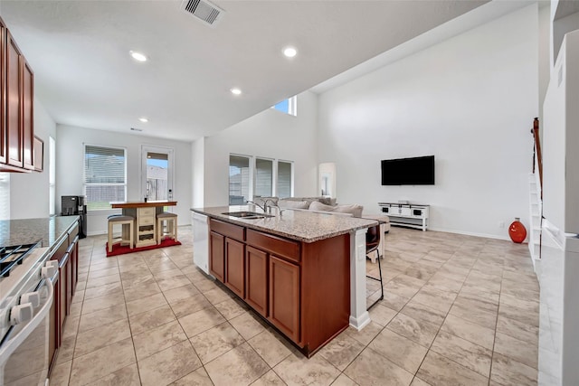 kitchen featuring light stone countertops, dishwasher, sink, stainless steel gas range oven, and an island with sink