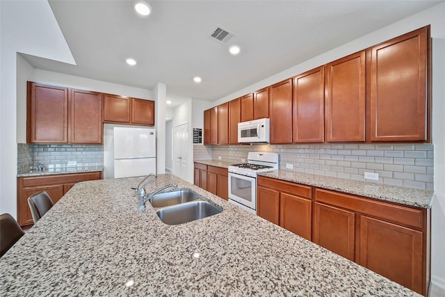 kitchen with a breakfast bar, white appliances, sink, decorative backsplash, and light stone countertops