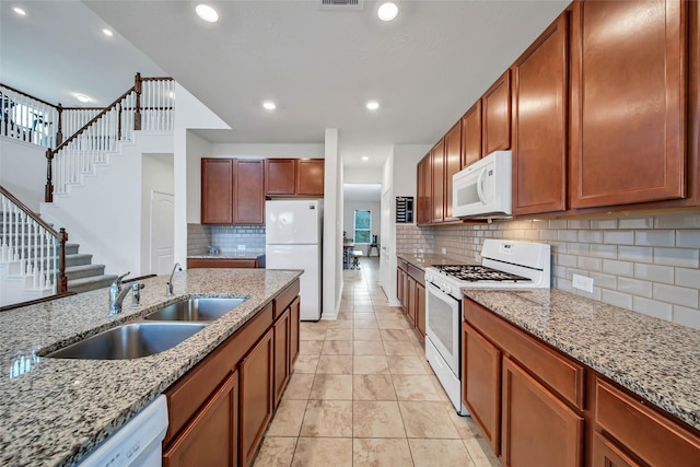 kitchen featuring light stone countertops, white appliances, backsplash, and sink