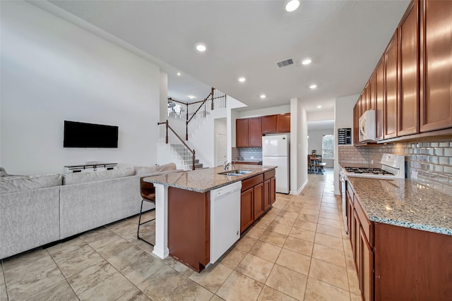 kitchen featuring light stone countertops, white appliances, a center island with sink, and backsplash