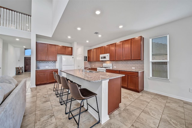 kitchen with sink, light stone counters, white appliances, a breakfast bar area, and a kitchen island with sink