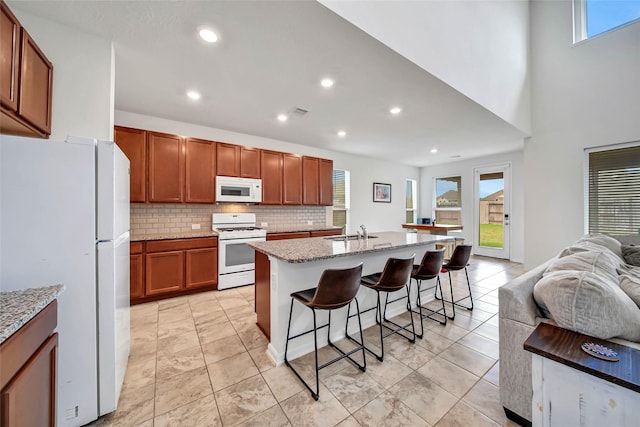 kitchen featuring a kitchen bar, white appliances, light stone countertops, and a kitchen island with sink