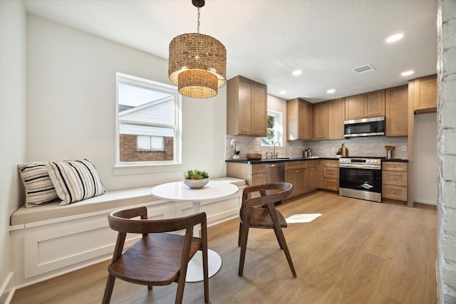 kitchen featuring backsplash, light wood-type flooring, hanging light fixtures, and appliances with stainless steel finishes