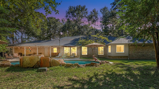 back house at dusk with an outdoor living space, a patio area, and a yard