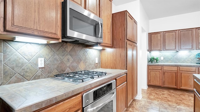 kitchen with tile countertops, backsplash, and appliances with stainless steel finishes