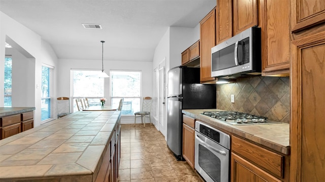 kitchen with pendant lighting, lofted ceiling, backsplash, tile counters, and stainless steel appliances