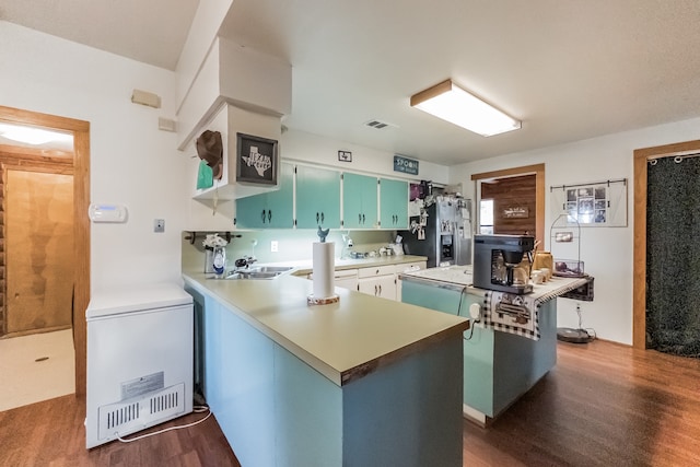 kitchen with dark wood-type flooring, stainless steel fridge with ice dispenser, kitchen peninsula, fridge, and a kitchen island