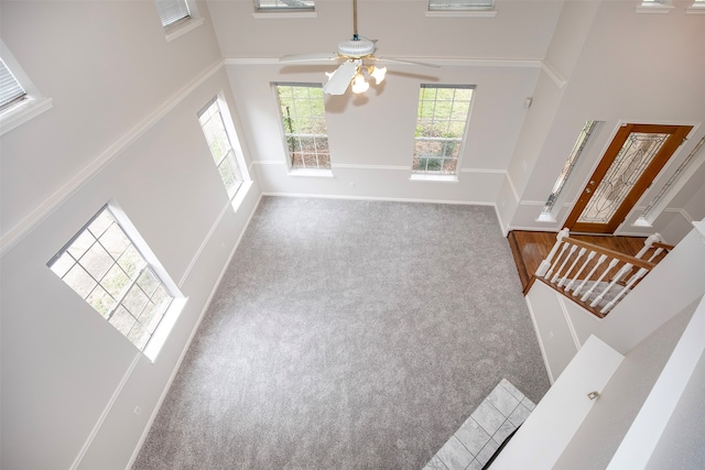 unfurnished living room featuring carpet, ceiling fan, crown molding, and a high ceiling