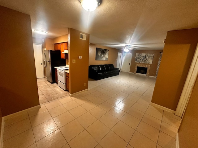 interior space featuring a textured ceiling, light tile patterned floors, white electric range, stainless steel refrigerator, and a tiled fireplace