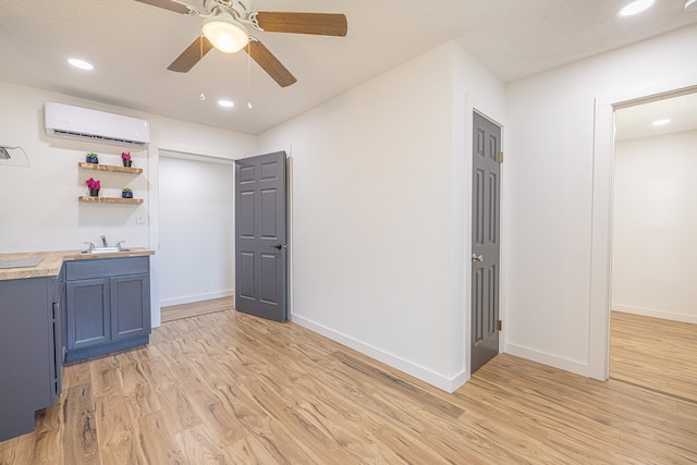 interior space with sink, light hardwood / wood-style flooring, ceiling fan, blue cabinetry, and a wall unit AC