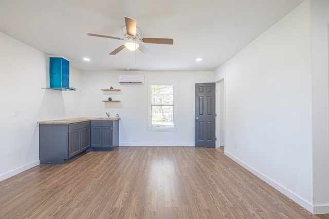 interior space featuring a wall unit AC, ceiling fan, blue cabinetry, and hardwood / wood-style flooring