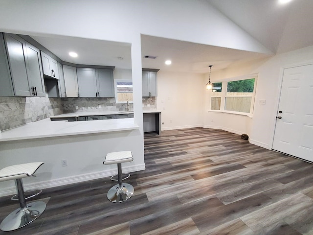 kitchen with kitchen peninsula, decorative backsplash, gray cabinetry, vaulted ceiling, and dark hardwood / wood-style floors