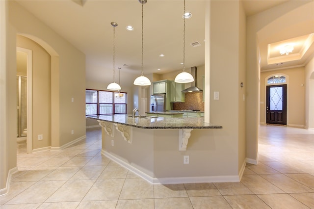 kitchen featuring stainless steel fridge, backsplash, a kitchen breakfast bar, wall chimney exhaust hood, and decorative light fixtures