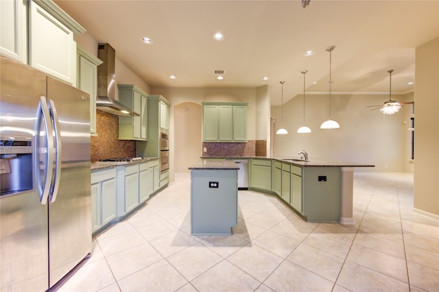 kitchen with appliances with stainless steel finishes, tasteful backsplash, wall chimney exhaust hood, sink, and decorative light fixtures