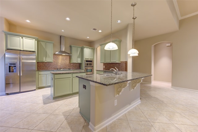 kitchen featuring wall chimney exhaust hood, stainless steel appliances, sink, dark stone countertops, and hanging light fixtures