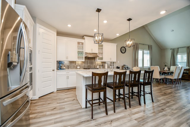 kitchen featuring appliances with stainless steel finishes, vaulted ceiling, pendant lighting, a center island with sink, and white cabinets