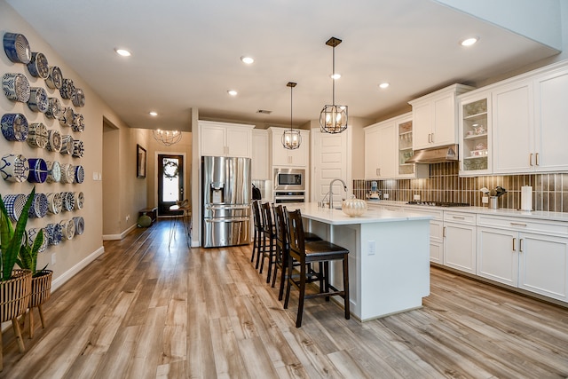 kitchen with white cabinetry, light hardwood / wood-style floors, pendant lighting, a center island with sink, and appliances with stainless steel finishes