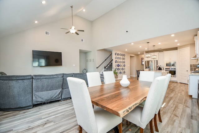 dining space with high vaulted ceiling, ceiling fan with notable chandelier, and light wood-type flooring