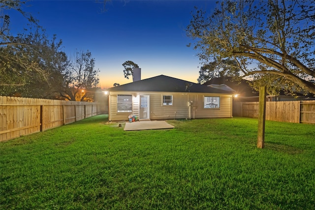 back house at dusk featuring a patio and a lawn