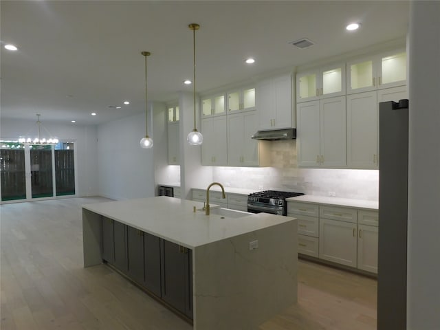 kitchen featuring stainless steel appliances, sink, decorative light fixtures, white cabinetry, and an island with sink