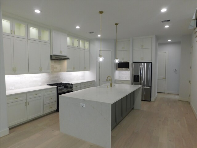 kitchen featuring white cabinets, an island with sink, stainless steel appliances, and light wood-type flooring