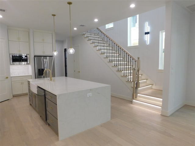 kitchen featuring white cabinets, appliances with stainless steel finishes, light wood-type flooring, and an island with sink