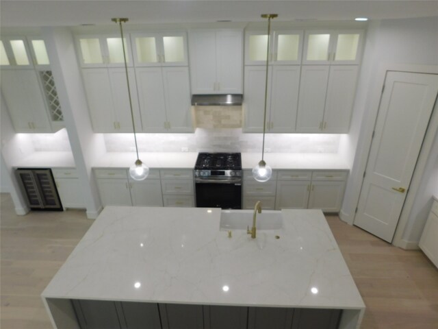 kitchen featuring stainless steel range with electric stovetop, a center island with sink, light stone countertops, and hanging light fixtures