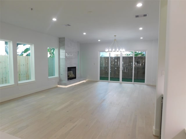 unfurnished living room featuring a notable chandelier, light wood-type flooring, and a fireplace