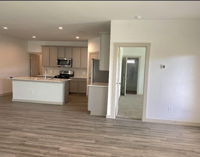 kitchen with gray cabinetry, backsplash, light hardwood / wood-style flooring, an island with sink, and appliances with stainless steel finishes