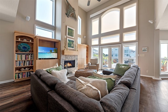 living room featuring a stone fireplace, dark wood-type flooring, and a high ceiling